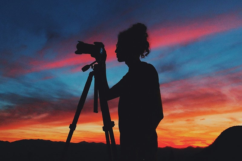 Силуэт ночной фотографии женщины с камерой на фоне красочного неба